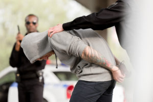 cropped shot of policewoman arresting male criminal in handcuffs while partner standing with handgun